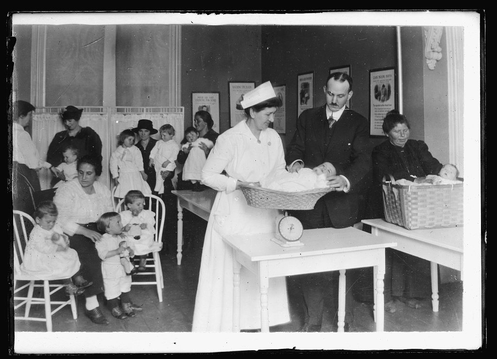 Weighing baby. Doctor and nurse at the American Red Cross Health Center at Hackensack, N.J., holding a clinic. The moth…