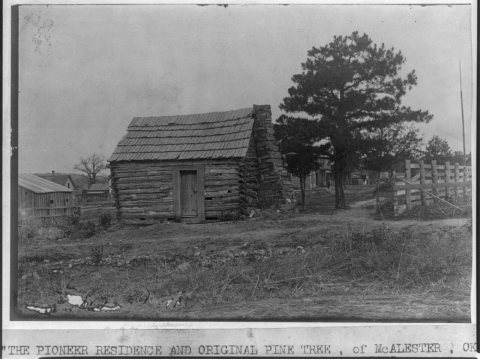 The Pioneer residence and original pine tree of McAlester, Okla., old log cabin in foreground