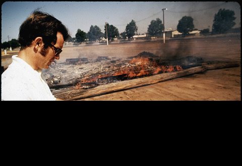 LOU DOOLEY, REGISTERED SANITARIAN WITH AIR POLLUTION CONTROL BOARD, CHECKS FIRE AT RODEO GROUNDS