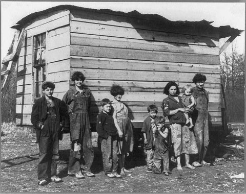 Family of nine living in open field in rough board covering built on old Ford truck chassis on U.S. Route 70, between B…