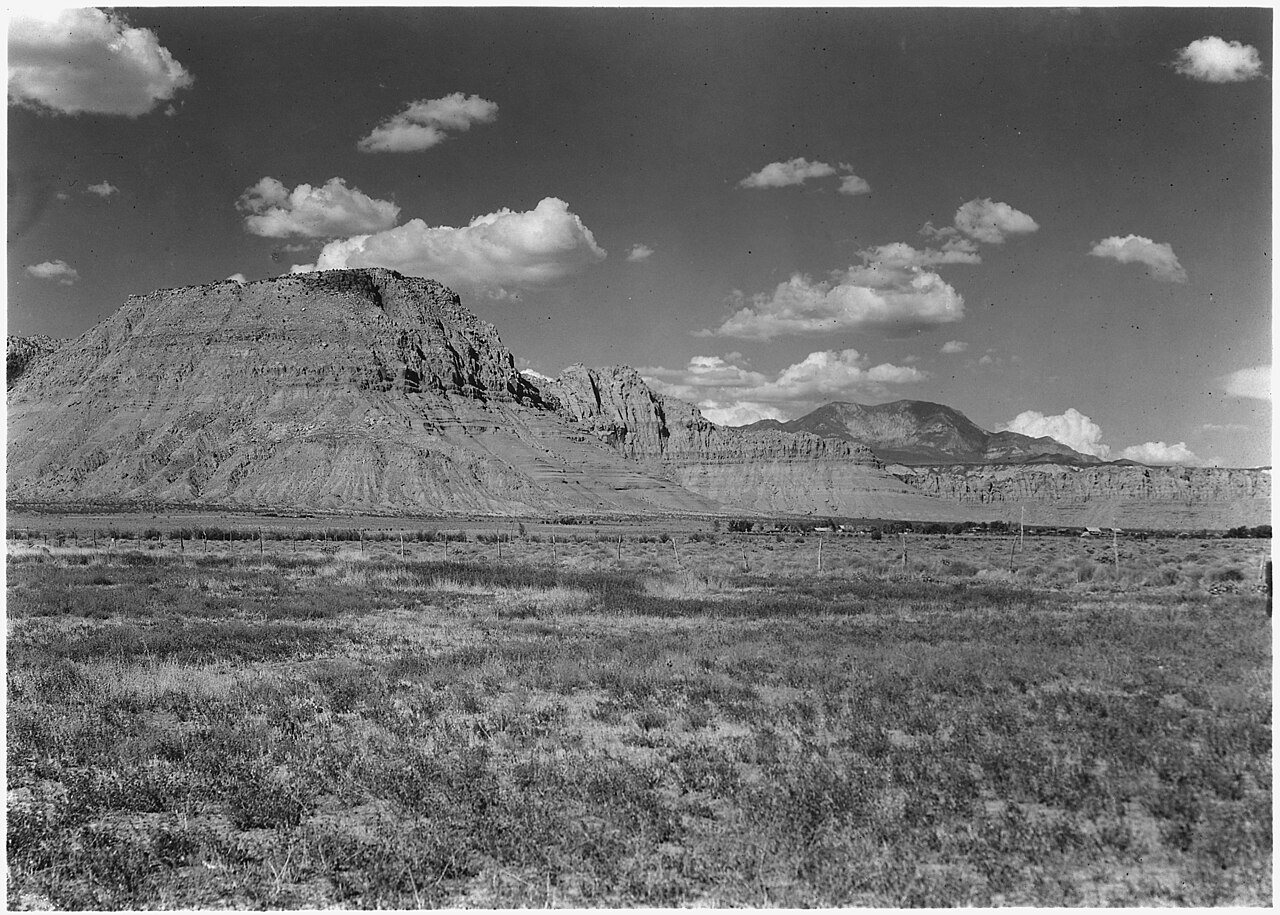 Front of Vermillion Cliffs. Village of Ivins, Utah, at base. Southern end of Pine Valley Mountain in distance at right
