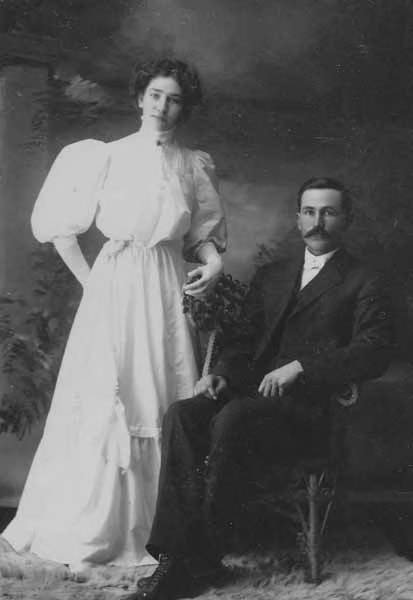 Woman in a white gown standing next to a seated man in a suit, Twisp, Washington, circa 1905-1910