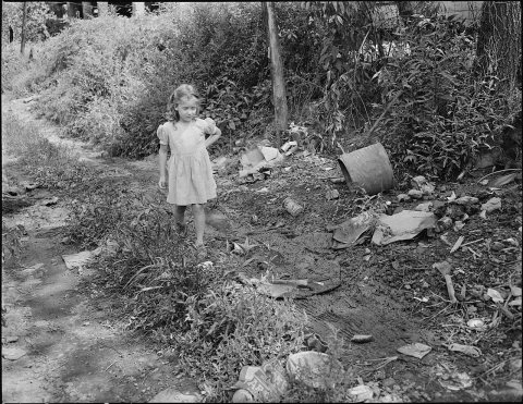 Child of miner walks down the road. This is all the street there is, there are no garbage collections and trash and... …