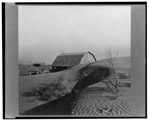The winds of the "dust bowl" have piled up large drifts of soil against this farmer's barn near Liberal, Kansas