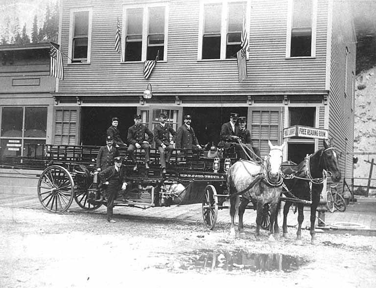 Wallace, Idaho Fire Department showing firemen in front of horse-drawn firetruck and firehouse, circa 1906