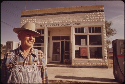 OWNER IN FRONT OF HIS GENERAL STORE IN ALAMO. M.K. STEWART IS ONE OF SEVERAL CITIZENS WHO WEARS A TLD... - NARA - 549019