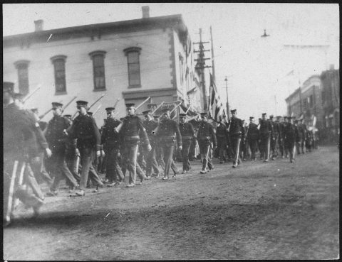 Photograph of men with rifles marching in parade