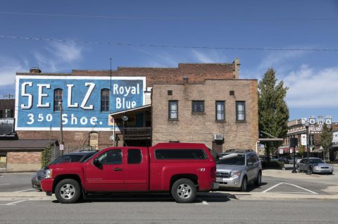 A strikingly red small truck provides a stark contrast to the blue antique mural, touting what was once a local shoesto…