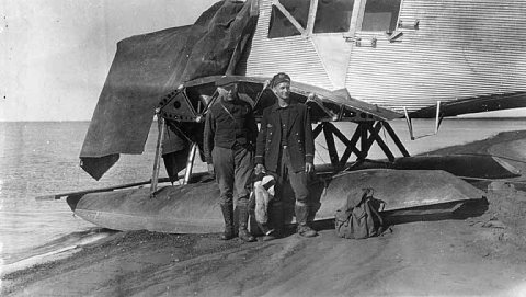 Roald Amundsen and a pilot standing in front of a seaplane on the beach at Wainwright, Alaska, 1922 or 1923