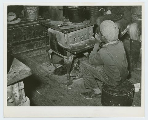 Negro boy sitting by the stove on a cold in the strawberry picking season near Independence, La. April 1939