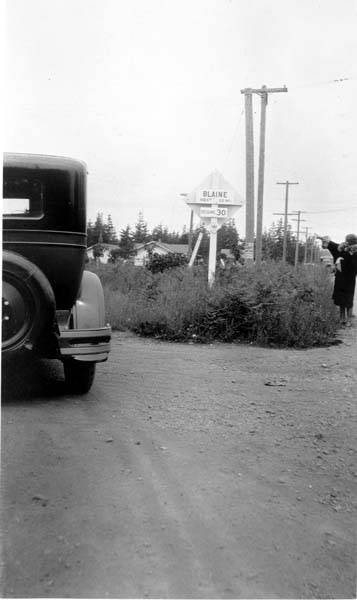 Woman pointing to road sign with automobile in view, Blaine, Washington, 1927